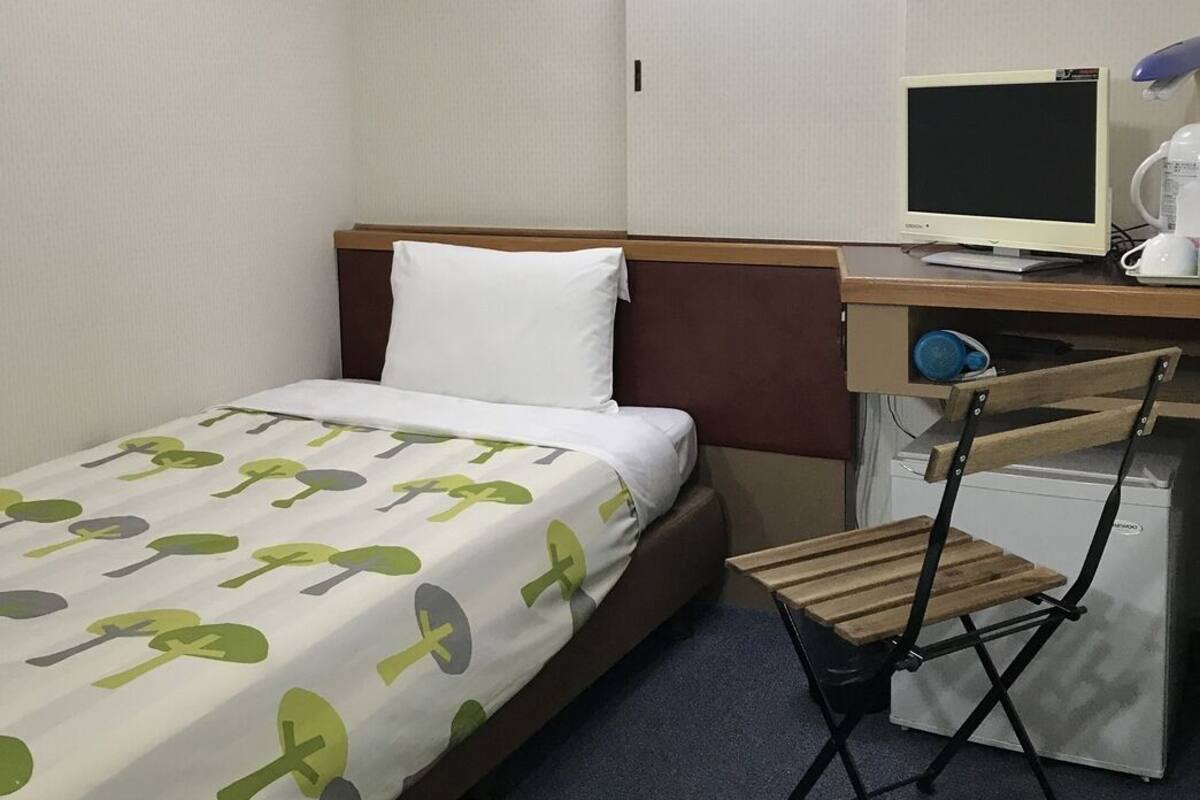 A hotel room with a bed, a desk with a computer, a chair, and a small refrigerator.