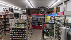 Interior de un supermercado con estantes llenos de diversos productos, un refrigerador de Coca-Cola y una caja registradora.