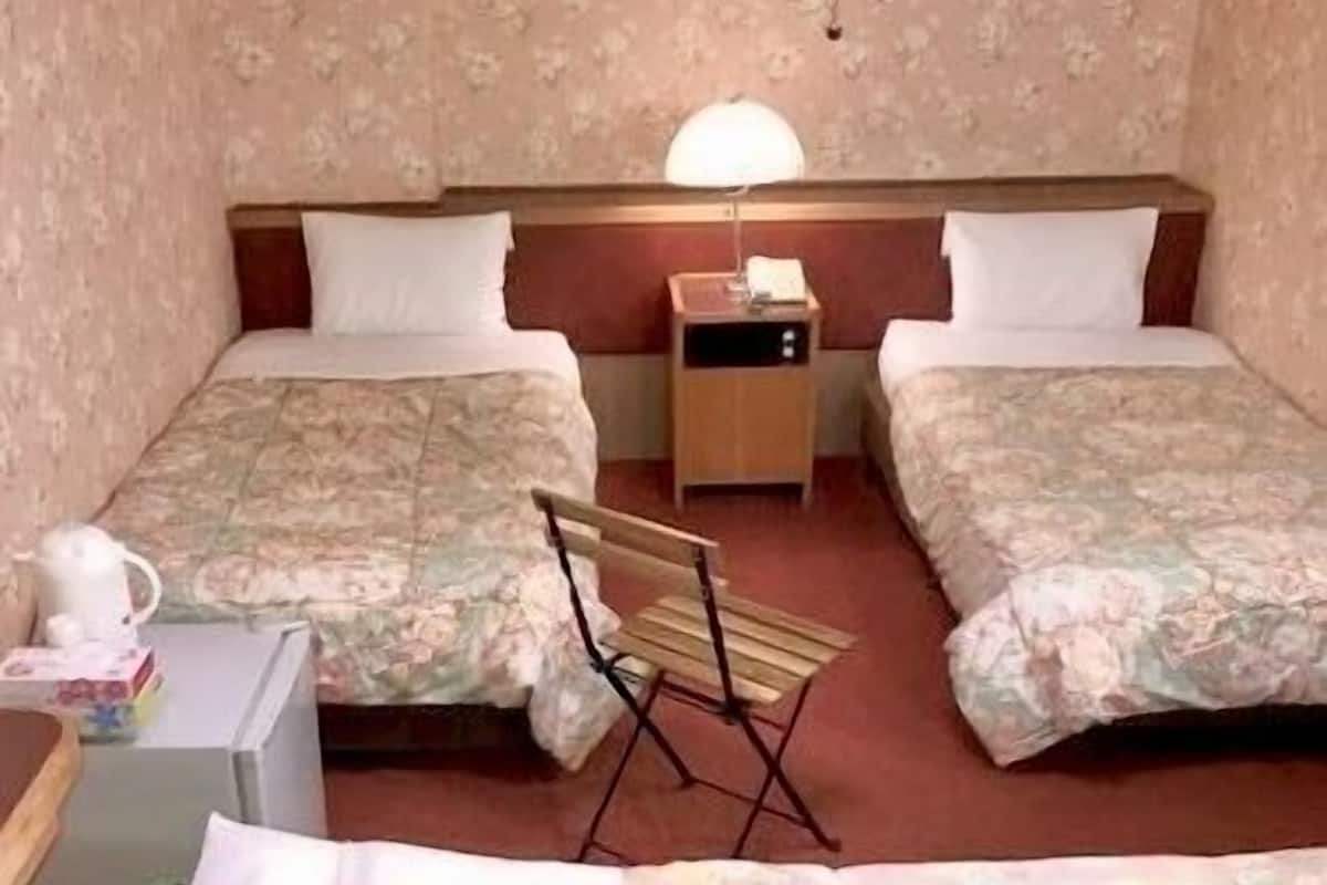 A double room with two beds, a nightstand, a lamp, and a folding chair.
