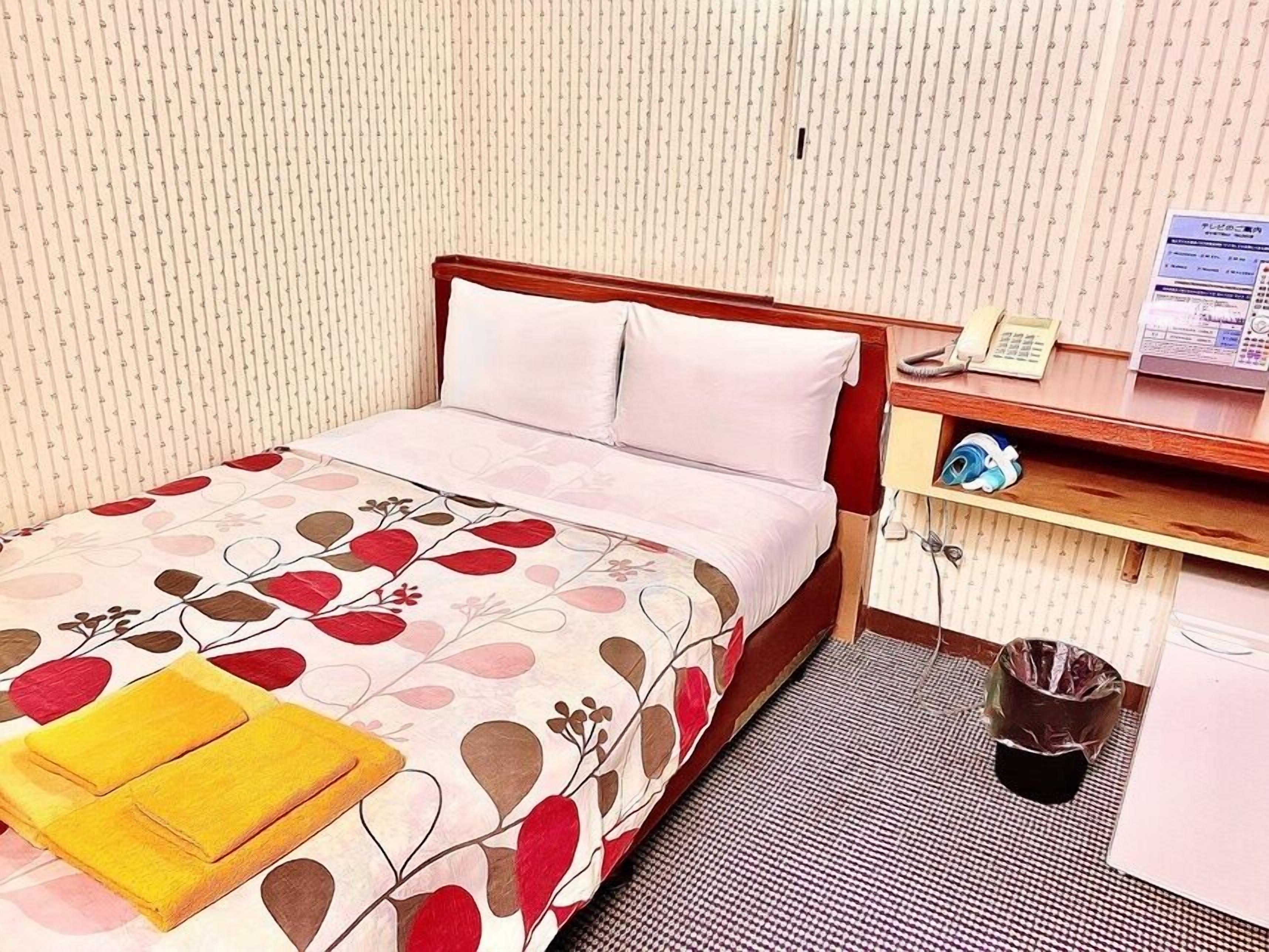 Habitación de hotel con cama, mesita de noche con teléfono, estante pequeño con artículos de aseo y un cubo de basura.