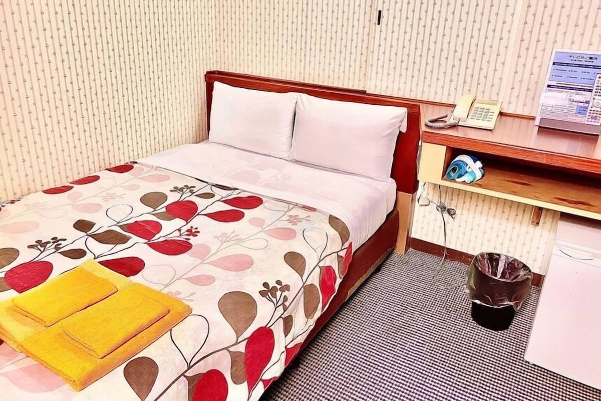 A hotel room with a bed, a bedside table with a telephone, a small shelf with toiletries, and a trash bin.