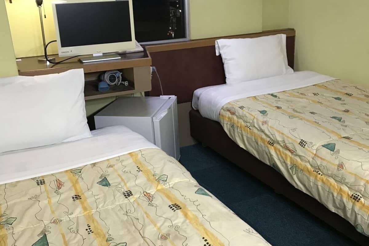 A hotel room with two beds, a desk with a computer, a lamp, and a window.
