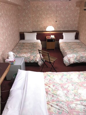 A hotel room with two beds, a desk, a chair, a small table, a nightstand with a lamp, and a telephone.
