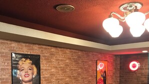 Una habitación con paredes de ladrillo, una lámpara en el techo, un cartel de Marilyn Monroe y un letrero de Coca-Cola.
