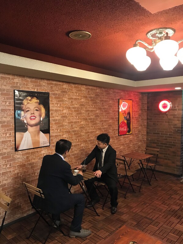 A brick-walled room with a ceiling light fixture, a poster of Marilyn Monroe, and a Coca-Cola sign.