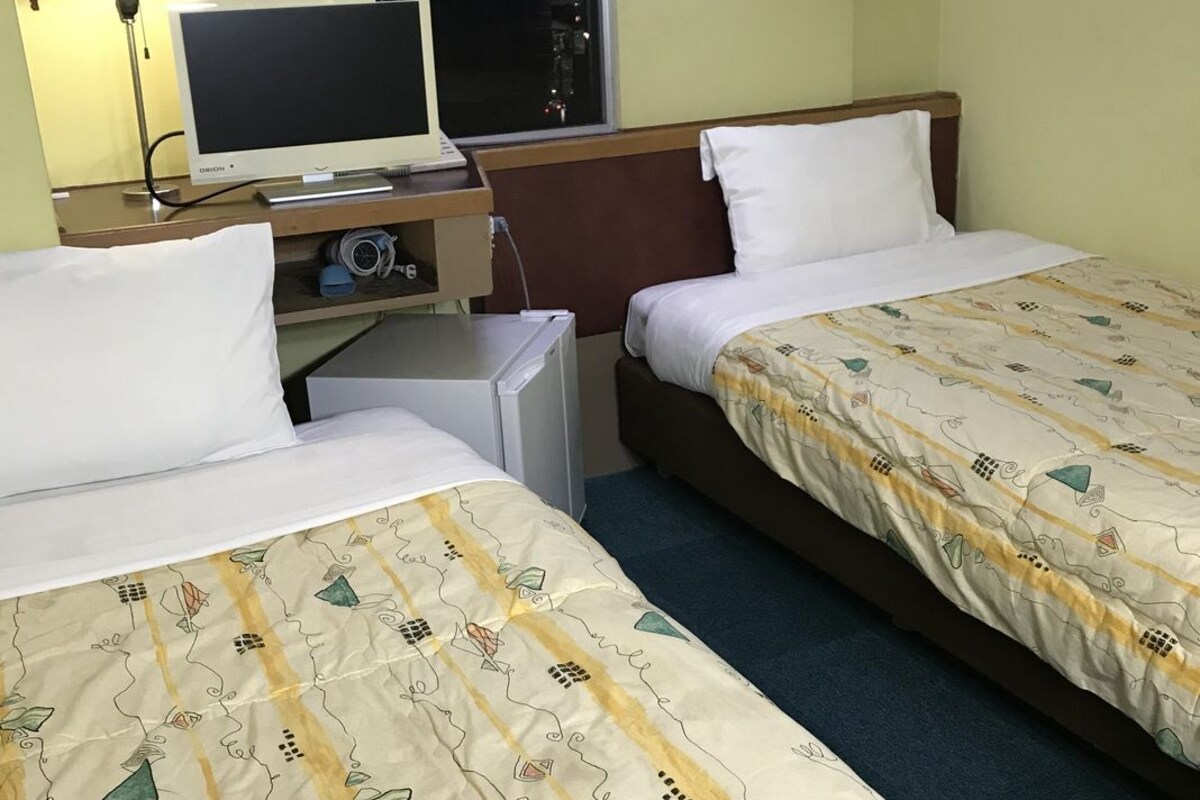 A hotel room with two beds, a desk with a computer, a lamp, and a window.