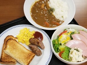 A meal consisting of toast, sausages, scrambled eggs, rice with gravy, and a salad with ham.