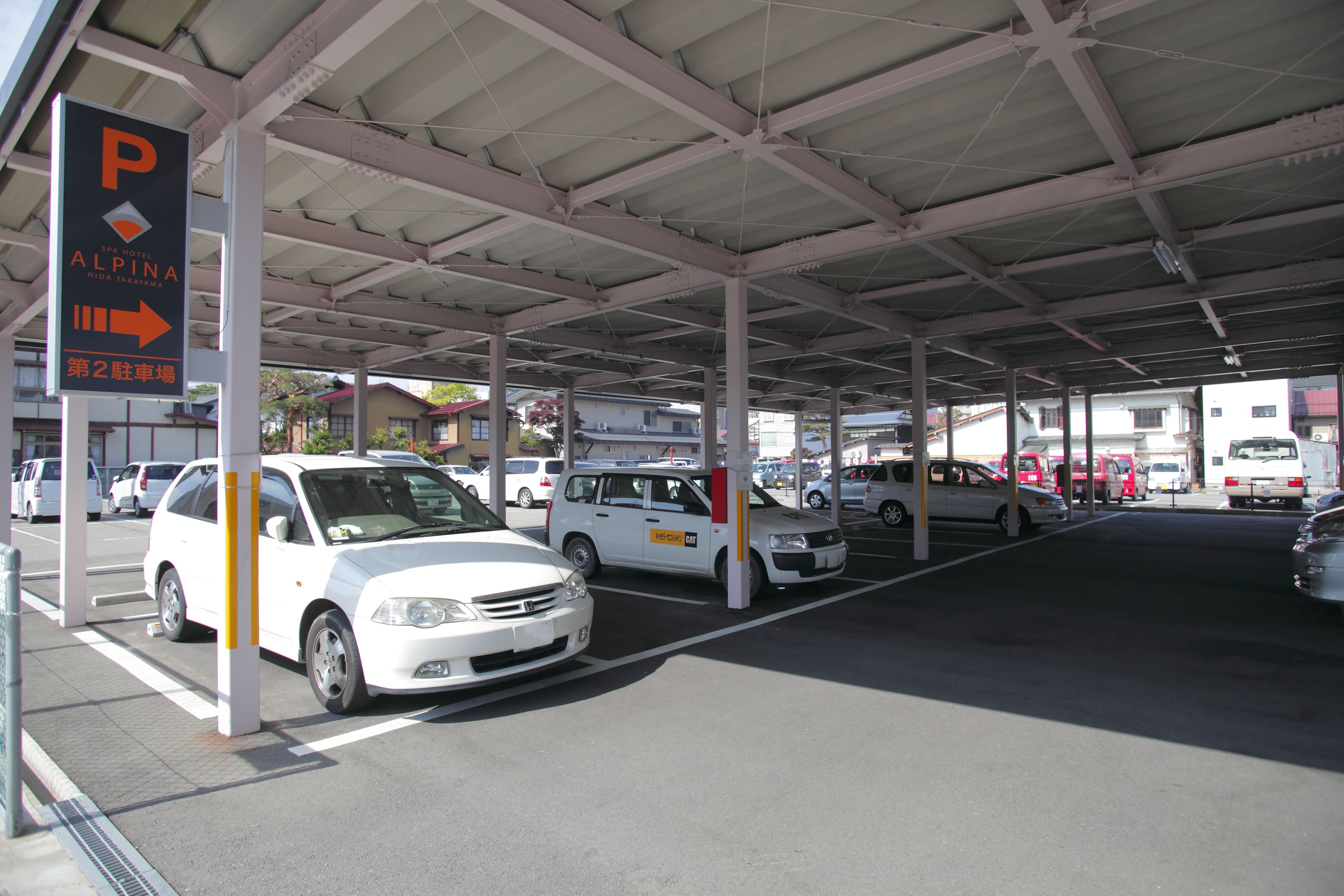 A parking area with a covered structure, multiple cars parked, and a sign indicating the direction to the second parking lot.