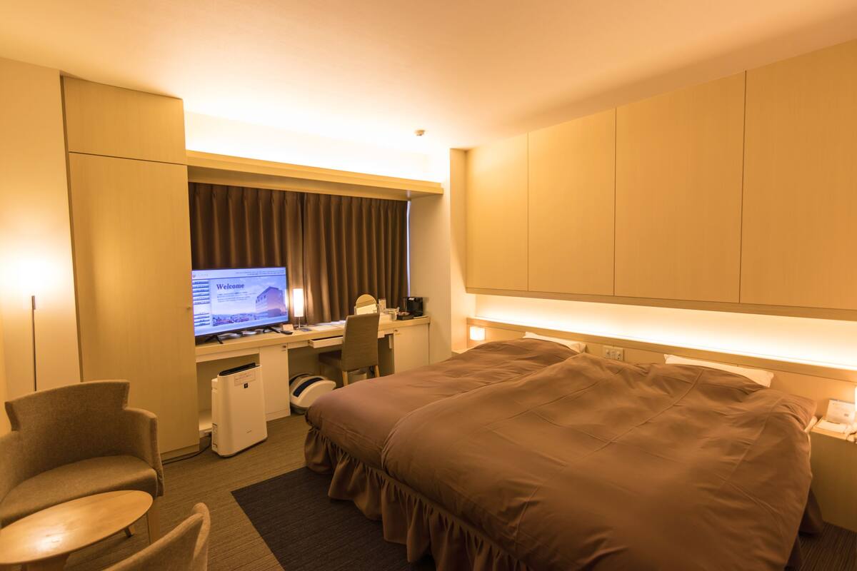 A hotel room with a bed, desk, chair, and a television displaying a welcome screen.