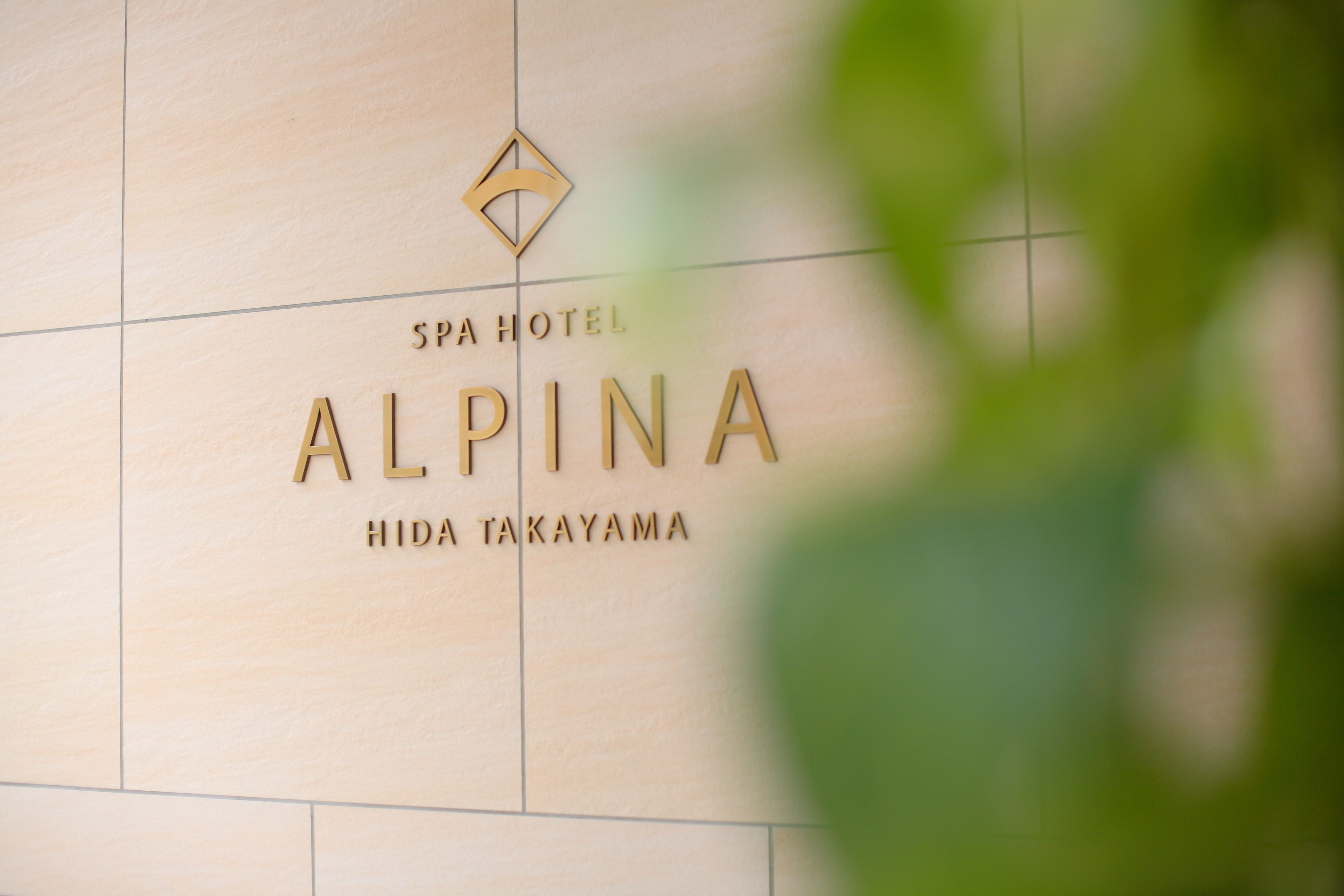 A sign for SPA HOTEL ALPINA HIDA TAKAYAMA with a geometric logo above the text.
