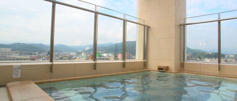 Una amplia piscina interior con vistas despejadas a montañas y a un paisaje urbano a través de grandes ventanales.