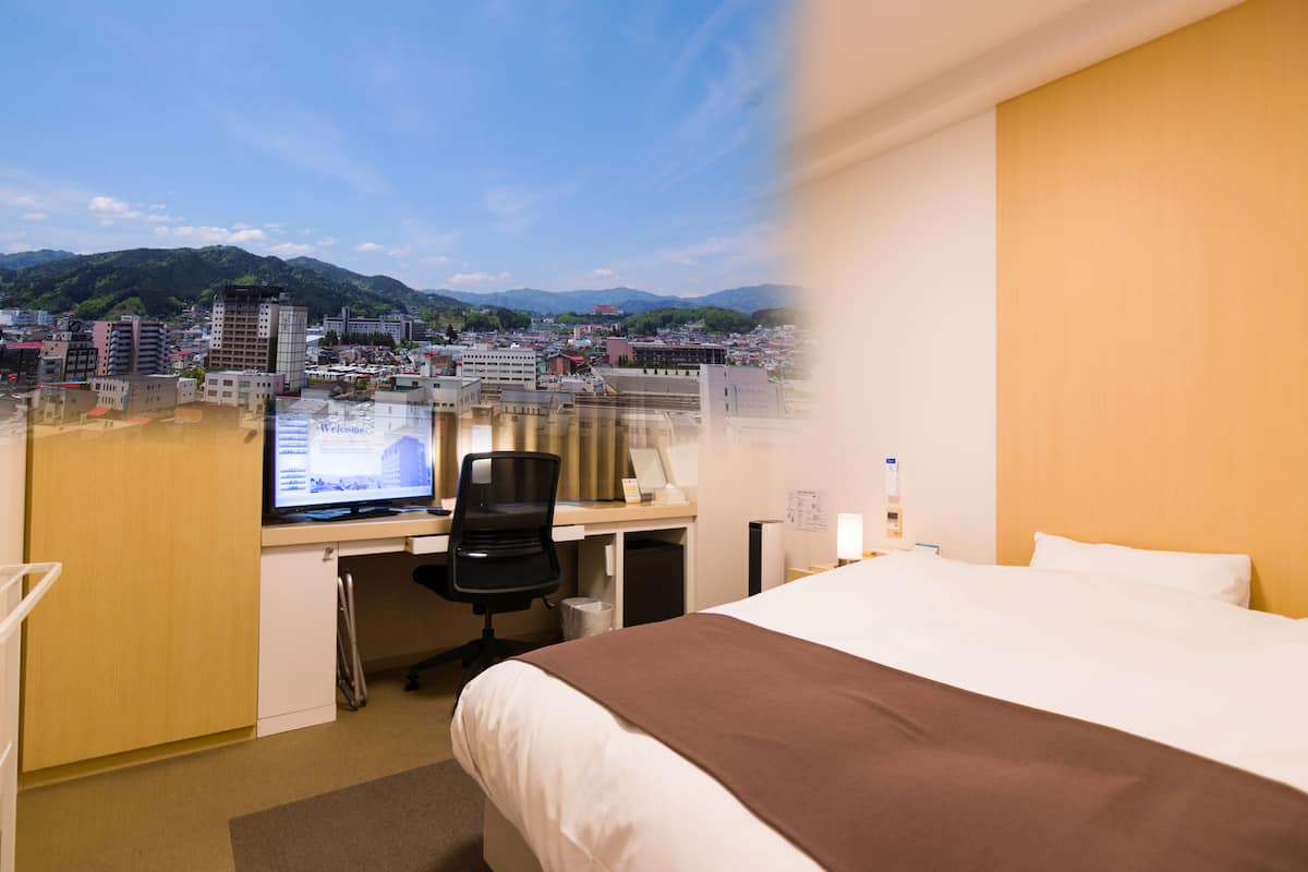 A hotel room with a bed, desk, and computer.