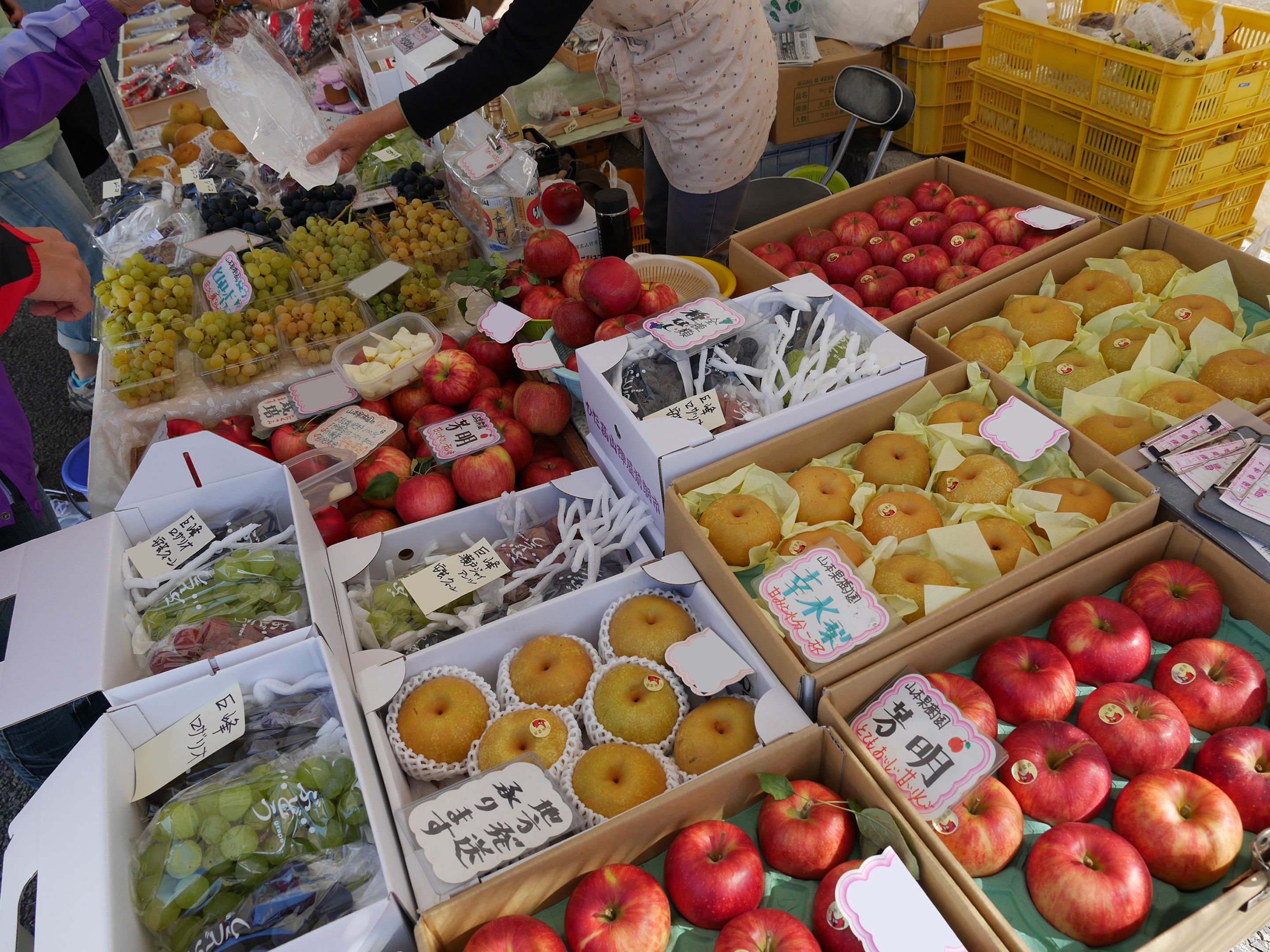 A market stall with various fruits and pastries, including apples, grapes, and donuts.