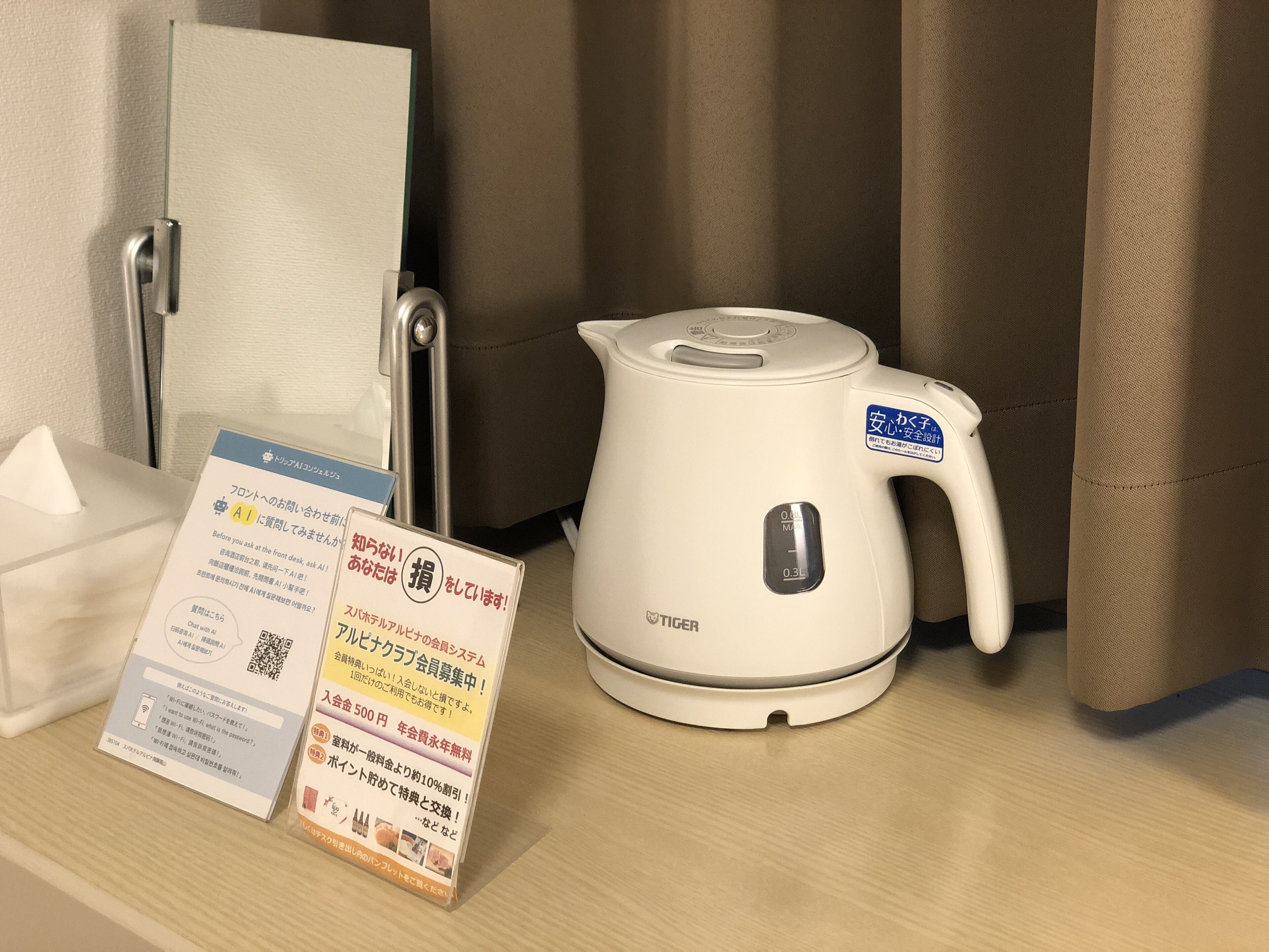 A white electric kettle with a digital display and a label, placed on a wooden surface next to a tissue box and a sign with Japanese text.