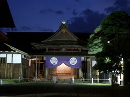 A traditional Japanese building with a tiled roof, wooden structure, and a purple banner with white designs.