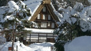 Une maison traditionnelle en bois, dotée d’un toit à forte pente recouvert de neige, et entourée d’arbres chargés de neige.