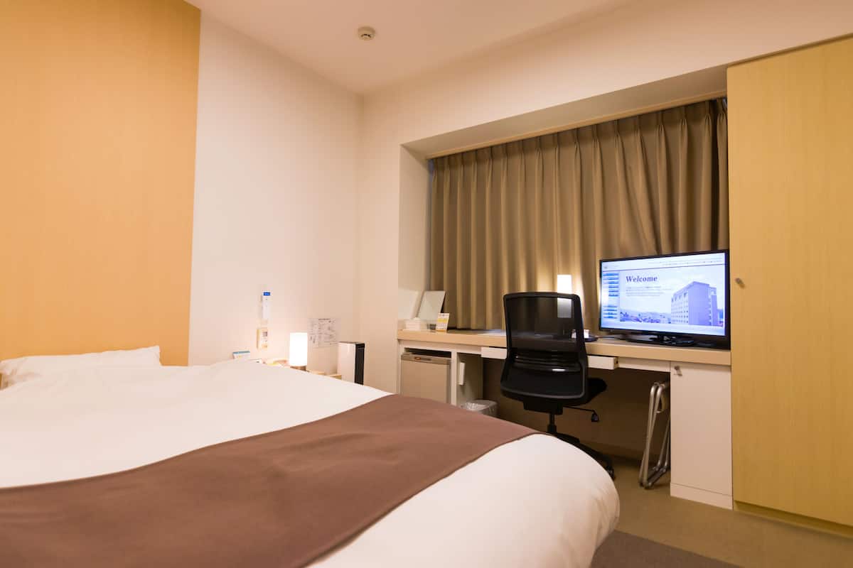 A hotel room with a large bed, a desk with a computer, and a wardrobe.