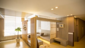 Une chambre d’hôtel moderne avec une cloison en bois, une plante en pot, un canapé et un petit coin salon avec des tabourets.