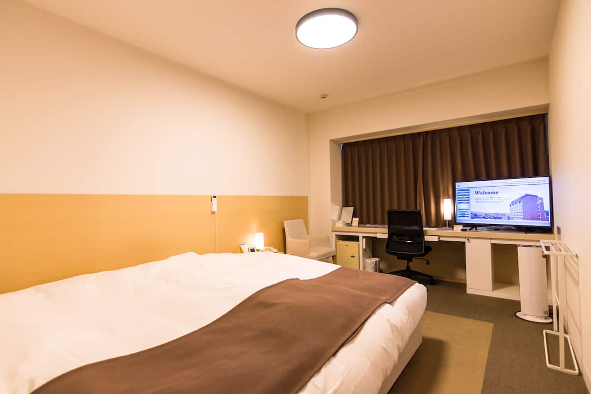 A hotel room with a large bed, a desk with a computer, and a television displaying a welcome screen.