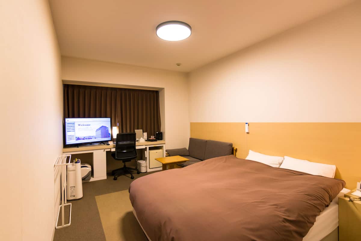 A hotel room with a bed, a desk, a computer, and a television.