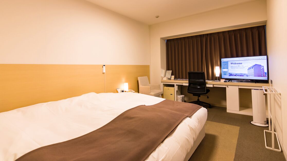 Camera d'albergo con un letto, una scrivania, una sedia, un computer e una televisione che mostra una schermata di benvenuto.