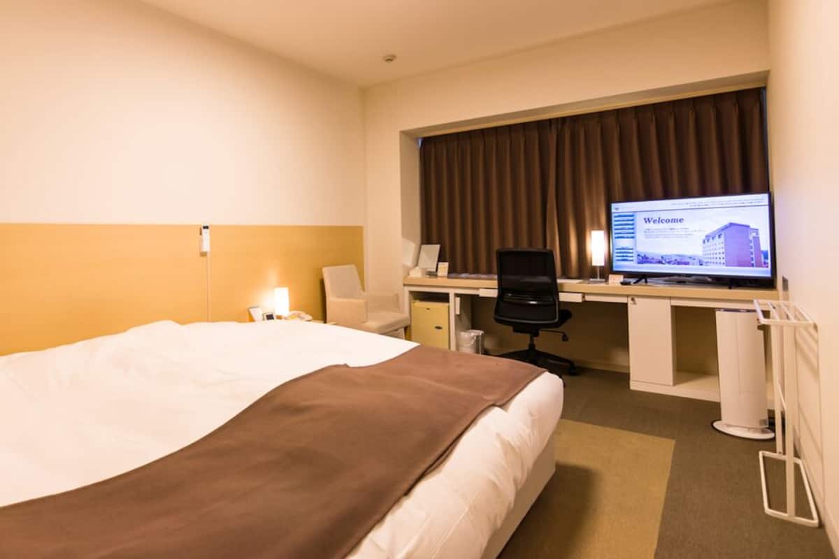 A hotel room with a bed, desk, chair, computer, and a television displaying a welcome screen.