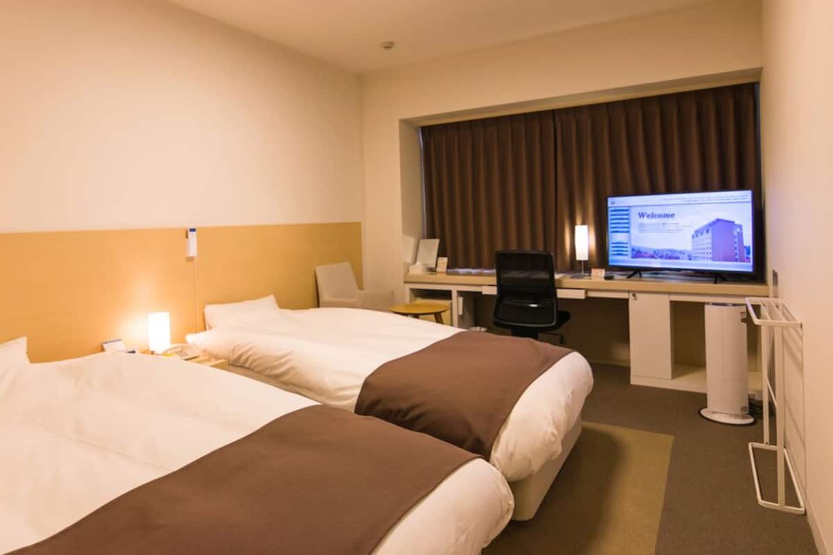 A hotel room with two beds, a desk, a computer, and a television displaying a welcome message.