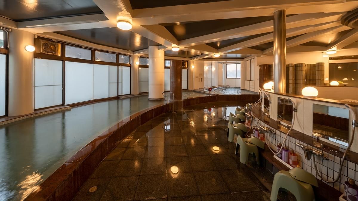 A spacious indoor swimming pool with a curved design, surrounded by seating areas and a sauna.