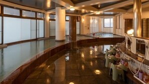 Un espacio interior amplio con suelo reflectante curvo, ventanas grandes y una zona de estar con taburetes.