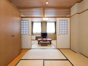 Ein traditioneller japanischer Raum mit Tatami-Böden, einem Fernseher und Schiebetüren.