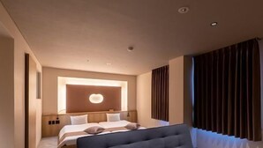 Habitación de hotel moderna con una cama grande, un sofá y un amplio ventanal con cortinas.