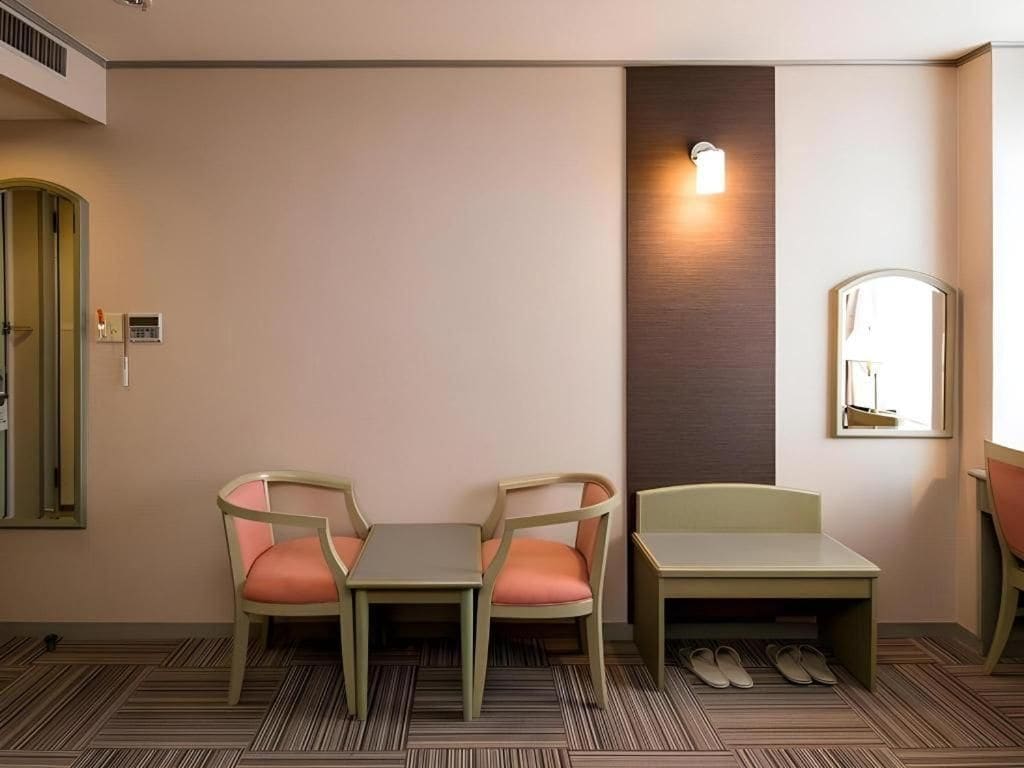 A hotel room with two chairs, a small table, a mirror, and a wall-mounted light fixture.