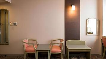 A hotel room with two chairs, a small table, a mirror, and a wall-mounted light fixture.