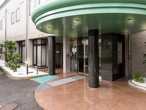 A hotel entrance with a curved glass canopy, a metal door, and a small outdoor area with a bench. - Ofuro Cafe New Biwako Hotel (Otsu)