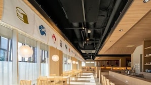 Un restaurante moderno con mesas y sillas de madera, una barra alargada e iluminación colgante.