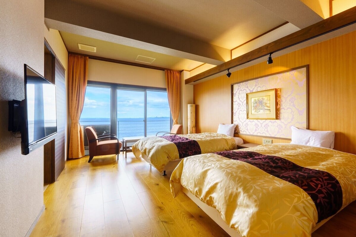 Une chambre d’hôtel avec deux lits, une télévision, une chaise et une grande fenêtre donnant sur un beau paysage.