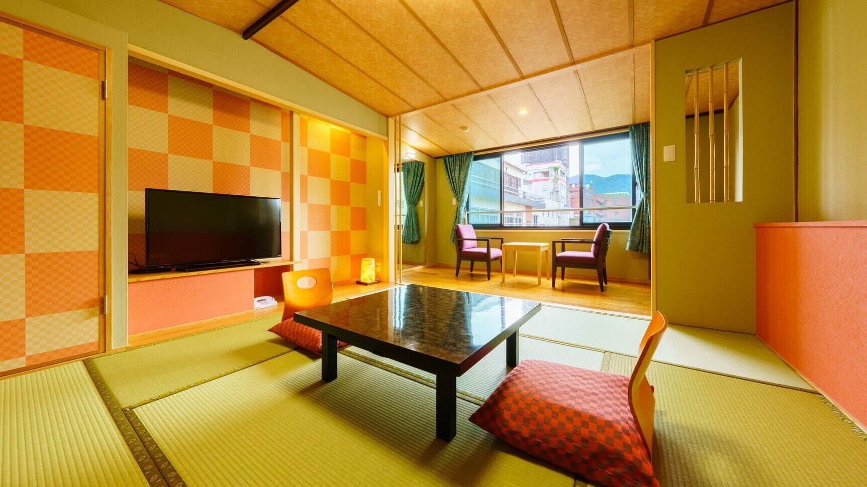 Quarto com tatames, televisão, mesa, cadeiras e vista para edifícios.