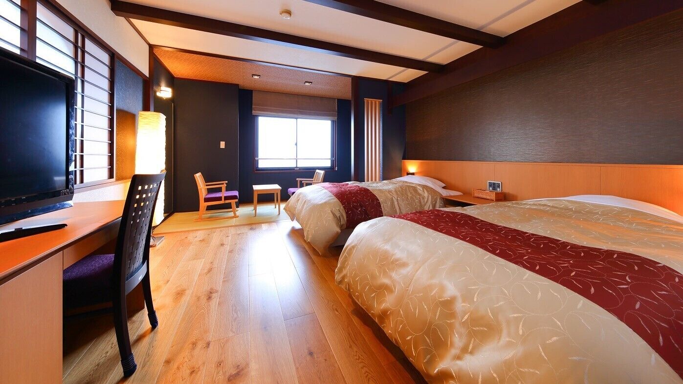 Une chambre d’hôtel avec deux lits, un bureau, une chaise et une grande fenêtre.