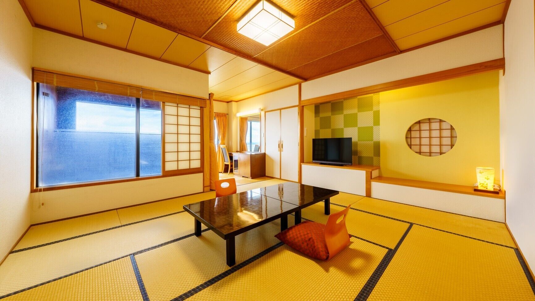Um espaço com esteiras de tatame, uma mesa baixa, almofadas, uma TV e vista para o mar.