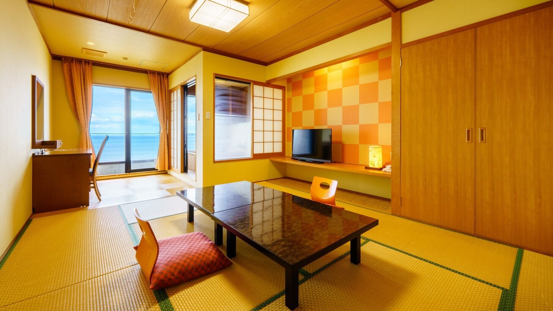 Um quarto japonês tradicional com tatames, uma porta deslizante para uma varanda, uma televisão e uma pequena mesa.