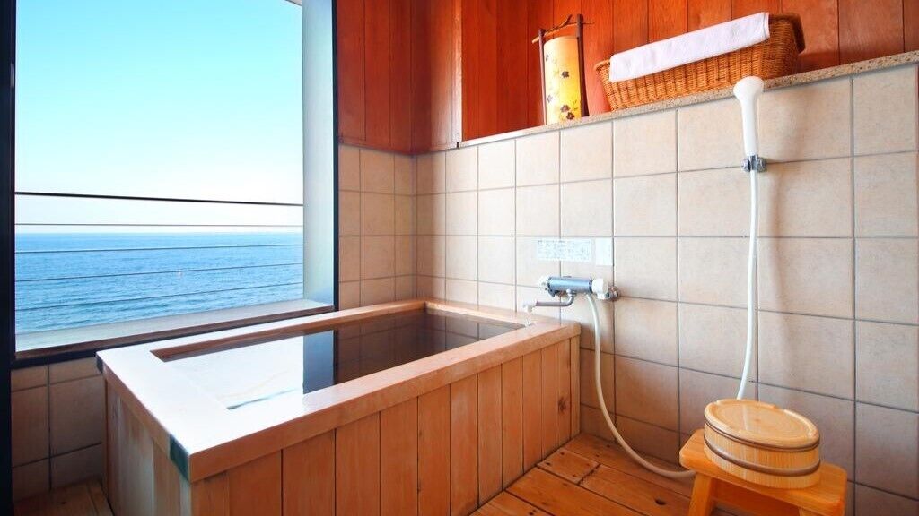 Une baignoire en bois donnant sur la mer, avec une fenêtre et un porte-serviettes.