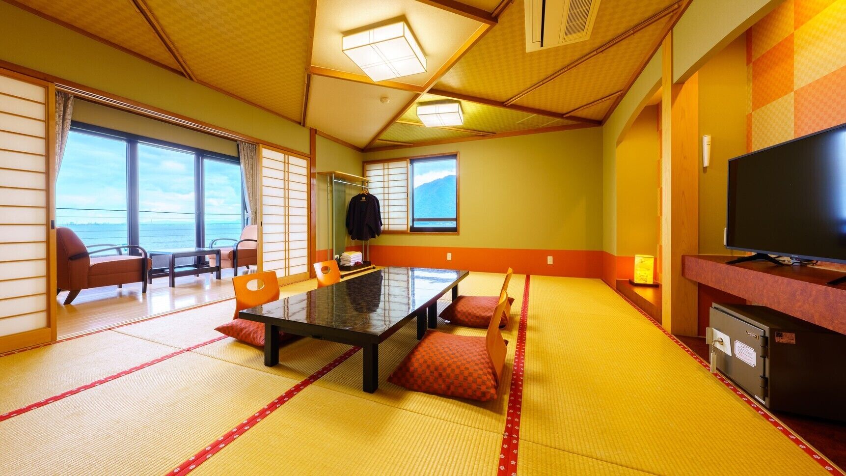 Um quarto com esteiras de tatame, uma mesa, cadeiras, uma televisão e vista para o mar.