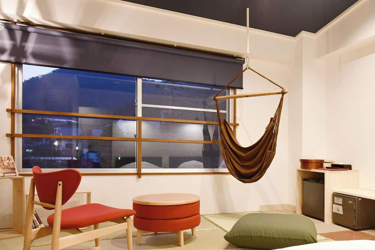 A modern room with a bed, a hanging chair, a small table, and a window with a view.