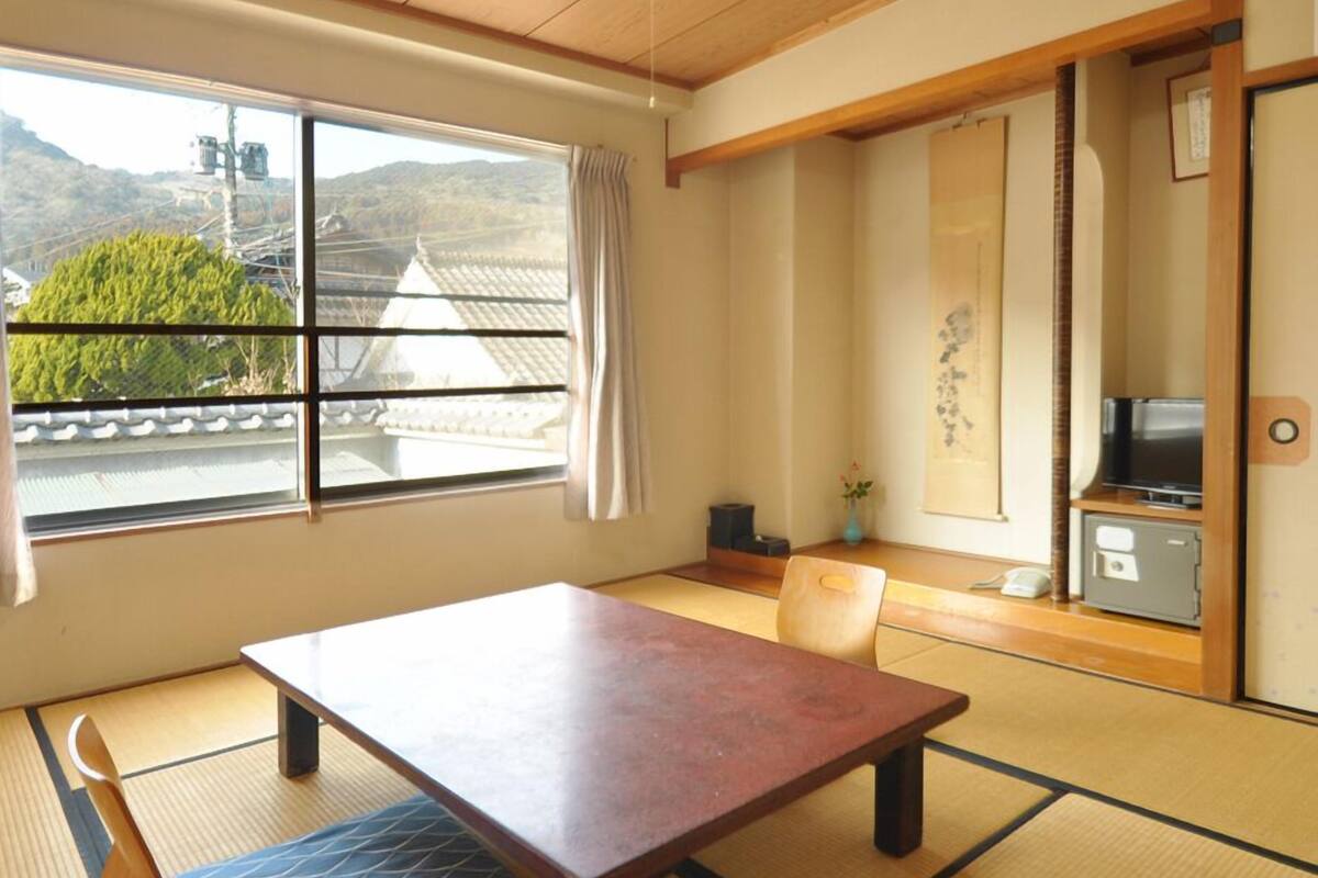 A traditional Japanese room with tatami flooring, a low table, a chair, a television, and a view of a mountain.