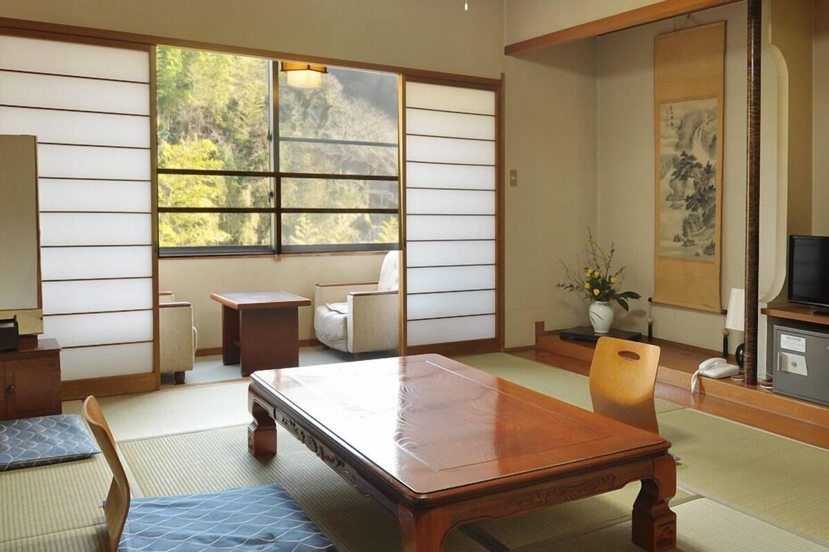 A traditional Japanese room with tatami flooring, a low wooden table, a sofa, and a television.