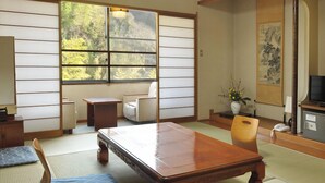 A traditional Japanese room with tatami flooring, a low wooden table, a sofa, a chair, a small side table, a TV, and a painting on the wall. - Ryokan Furuyu Onsen Ogiya (SAGA SHI)