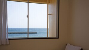 Una habitación con cama, ventana con vista al mar y cabecero de madera.