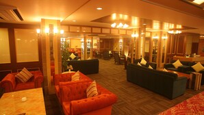 Un hall de hotel con varias zonas de estar, incluyendo sofás naranja y verde, un mostrador de recepción y una pared grande con espejos.