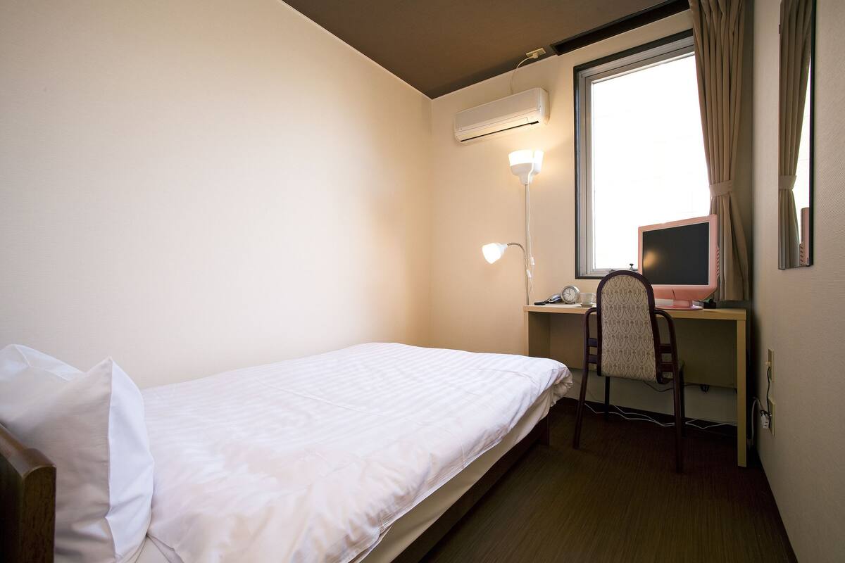 A small hotel room with a single bed, a desk with a computer, and a window with curtains.