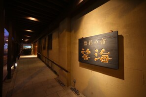 A corridor with a wooden signboard displaying Japanese characters, a tiled floor, and a railing along the walkway. - Bokai Hotel (Beppu)